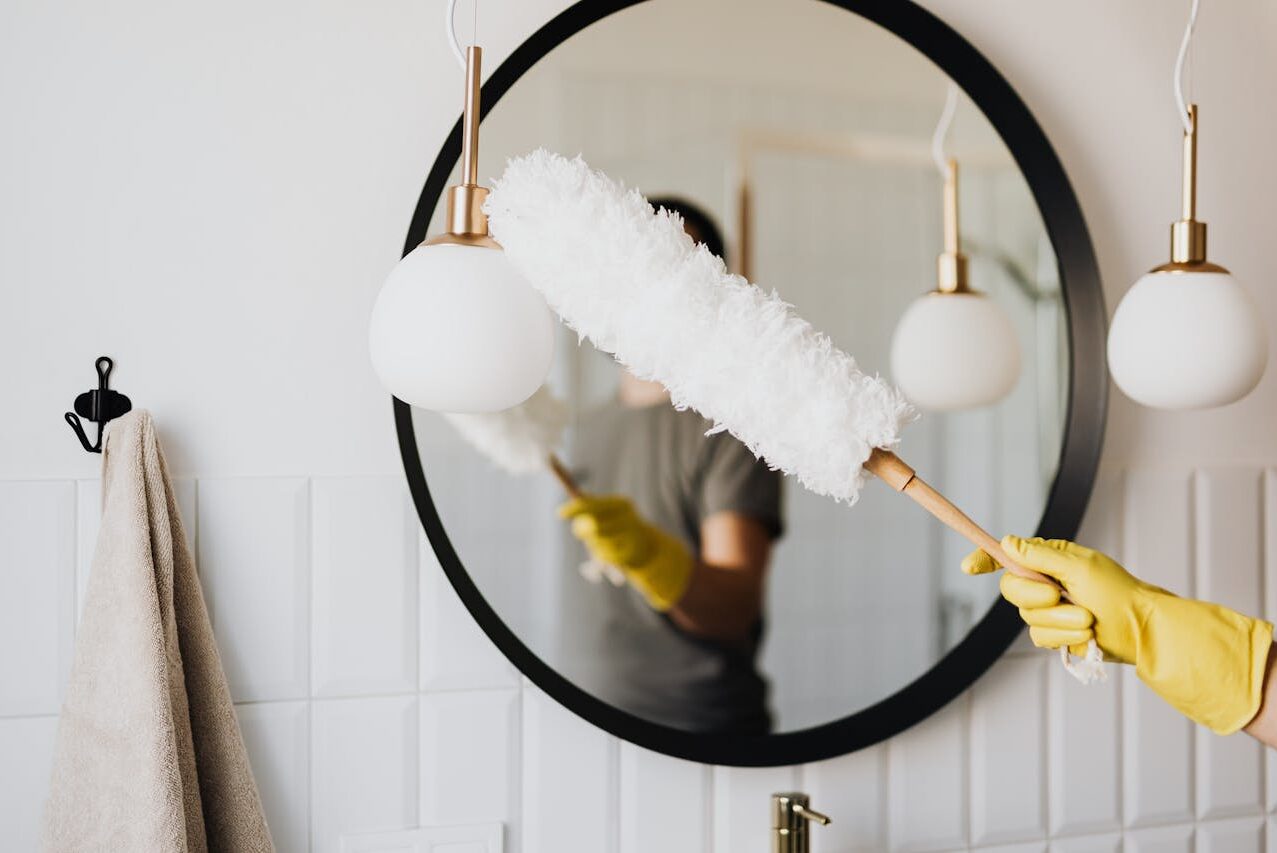 pexels photo 4239031 A person cleaning an elegant bathroom mirror with a fluffy duster and yellow gloves.